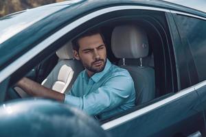 Driving his brand new car. Handsome young man in smart casual wear looking away while driving a status car photo