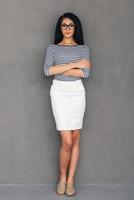 Confident beauty. Full length of beautiful young African woman looking at camera and keeping arms crossed while standing against grey background photo