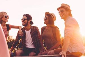 Road trip with best friends. Group of young cheerful people enjoying their road trip while sitting in pick-up truck together photo