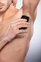 Clean and fresh. Cropped image of young shirtless man using dry deodorant while standing isolated on grey background photo