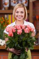 floristería con ramo de rosas. hermosa joven rubia en delantal sosteniendo un ramo de rosas y sonriendo foto