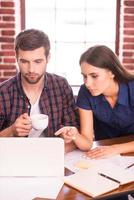 Working on project together. Confident young man and woman sitting at the working place together while woman pointing laptop photo
