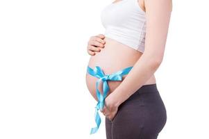 Waiting for a baby. Side view cropped image of pregnant woman with blue ribbon on her belly standing isolated on white photo