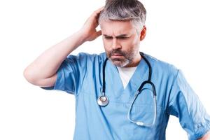 Depressed surgeon. Side view of depressed mature doctor touching his face with hand and keeping eyes closed while standing isolated on white photo