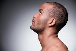 confianza y masculinidad. vista lateral de un joven africano sin camisa mirando hacia arriba mientras se enfrenta a un fondo gris foto