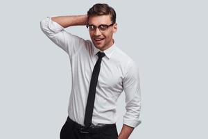 Confident and successful. Good looking young man smiling and keeping hand behind head while standing against grey background photo