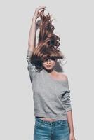 Confident in her healthy hair. Attractive young woman stretching her hair up and while standing against grey background photo