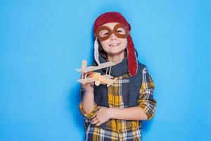 Dreaming of a big sky. Thoughtful of little boy in helmet playing with toy plane while standing against blue background photo