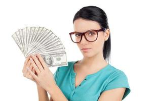 Rich and confident. Confident young woman in glasses holding money in her hands and looking at camera while standing isolated on white photo