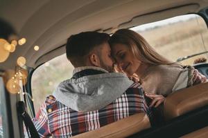 él nunca la dejará ir. hermosa pareja joven sonriendo mientras se sienta cara a cara en los asientos del pasajero delantero en una mini furgoneta de estilo retro foto