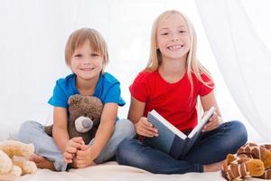 We love spending time together. Two cute children smiling while sitting together on bed photo