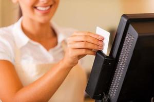 Cashier at work. Close-up of beautiful young female cashier swipes a plastic card through a machine photo