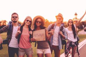 Friends hitchhiking. Beautiful young people with backpacks hitchhiking on the road and looking happy photo