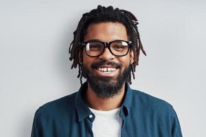 Handsome young African man in eyewear looking at camera and smiling while standing against grey background photo