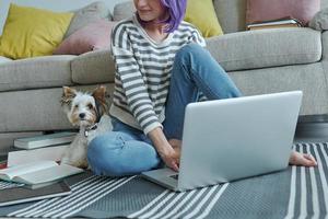 primer plano de una adolescente usando una laptop en casa mientras su perrito se sienta cerca de ella foto