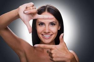 sonríe para el retrato de la cámara de una joven feliz sin camisa mirando la cámara y gesticulando con el dedo mientras se enfrenta a un fondo gris foto