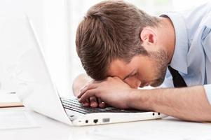 Tired and overworked. Side view of young man in shirt and tie sleeping while sitting at his working place photo