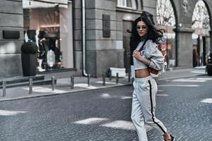 Enjoying nice day. Beautiful young woman carrying fashionable backpack while walking outdoors photo