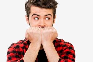 Can not keep emotions inside. Nervous young man biting nails and looking away while standing against white background photo