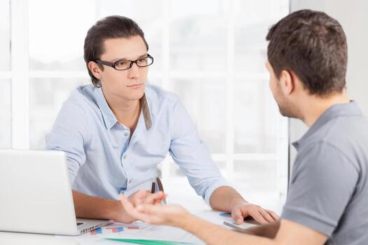 Trying to find solution. Two confident business people in casual wear discussing something and gesturing while sitting at the table photo
