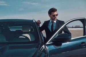 Luxury style. Handsome young businessman entering his car while standing outdoors photo