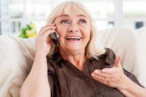 buena plática. anciana alegre hablando por teléfono móvil y gesticulando mientras se sienta en una silla foto