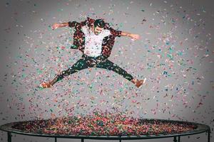 Fun in motion. Mid-air shot of handsome young man jumping on trampoline with confetti all around him photo