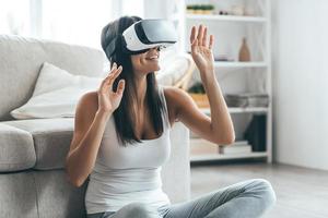 Testing her new VR headset. Attractive young woman in VR headset gesturing and smiling while sitting at home photo