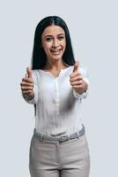 Success achieved Happy young attractive woman in white shirt gesturing and smiling while standing against grey background photo