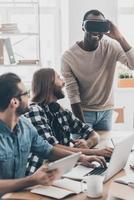 realidad diferente. el equipo de desarrollo coopera en su oficina mientras un joven apuesto ajusta los auriculares vr y sonríe foto