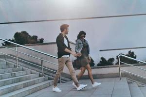 Enjoying time together. Full length of handsome man and young attractive woman holding hands while walking down the stairs outdoors photo
