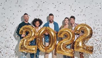 Group of young beautiful people in casual clothing carrying gold colored numbers  and smiling photo