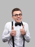 Everything is good. Portrait of young nerd man in bow tie and suspenders looking at camera and gesturing while standing against grey background photo