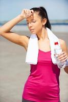 relajarse después de trotar. mujer joven cansada bebiendo agua y manteniendo los ojos cerrados mientras está de pie al aire libre foto