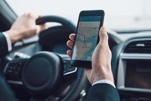 Searching for the shortest way. Close up of young man using smart phone to check the map while driving a car photo