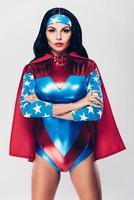 Gorgeous and powerful. Beautiful young woman in superhero costume looking at camera and keeping arms crossed while standing against white background photo