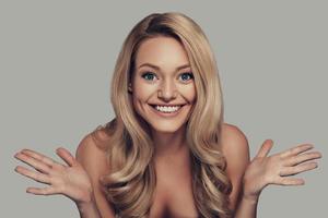 Beautiful perfection. Beautiful young woman smiling and looking at camera while standing against grey background photo