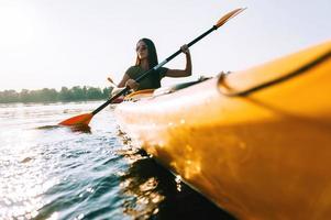 Looking for adventures. Low angle view of beautiful young smiling woman kayaking on lake and smiling photo