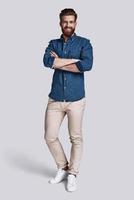 Confident in his style. Full length of handsome young man looking at camera and keeping arms crossed while standing against grey background photo