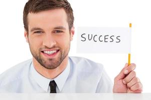 Success Handsome young man in shirt and tie holding flag with success text on it while looking out of the table photo