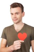I guess I am in love. Handsome young man holding a paper heart and smiling while standing isolated on white background photo