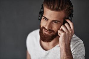 Music therapy.  Top view of good looking young man listening music while standing against grey background photo