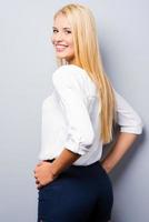 Confident beauty. Rear view of beautiful young women looking at camera and holding hands on hip while standing against grey background photo