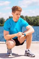 Getting ready to jogging. Handsome man checking time before jogging on riverbank photo