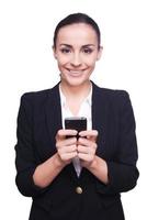 Business lady with mobile phone. Cheerful young woman in formalwear holding mobile phone and smiling while standing isolated on white photo