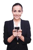 mujer de negocios con teléfono móvil. mujer joven alegre en ropa formal sosteniendo teléfono móvil y sonriendo mientras está de pie aislado en blanco foto