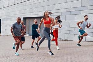 toda la longitud de los jóvenes con ropa deportiva trotando mientras hacen ejercicio en la acera al aire libre foto