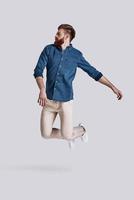 Feeling free to do anything.  Full length of handsome young man keeping eyes closed while jumping against grey background photo