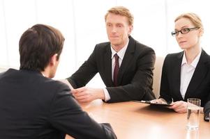 Job interview. Rear view of young man in formalwear sitting in front of two another business people photo