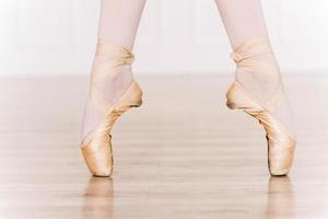 Elegance in every move. Close-up of ballerina legs in white tutu and slippers photo